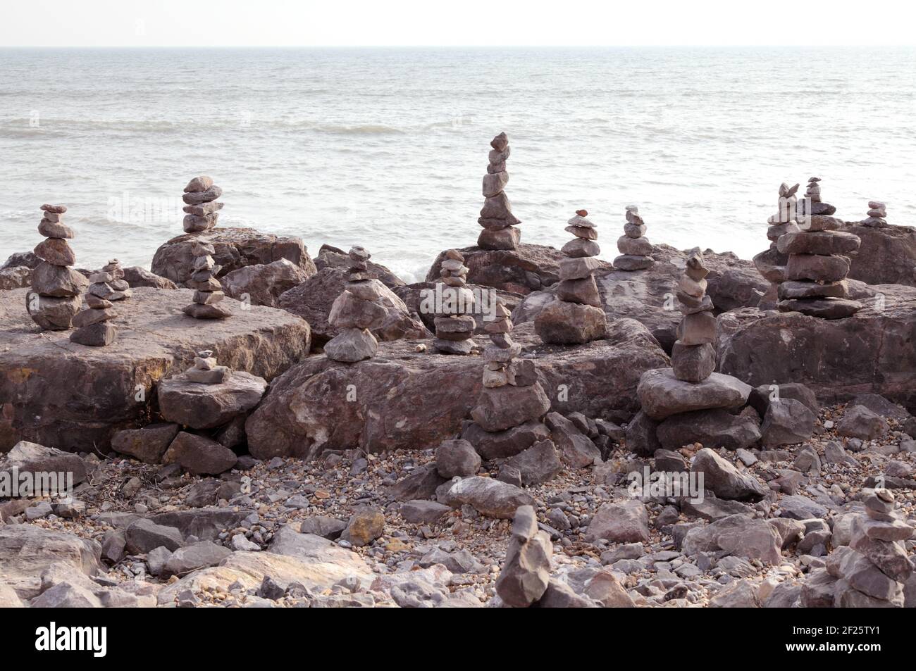 Pile di pietre equilibranti o rocce bilanciate per fare la roccia o la pietra cairns. Accatastato o accatastato sulla spiaggia con il mare dietro. Foto Stock
