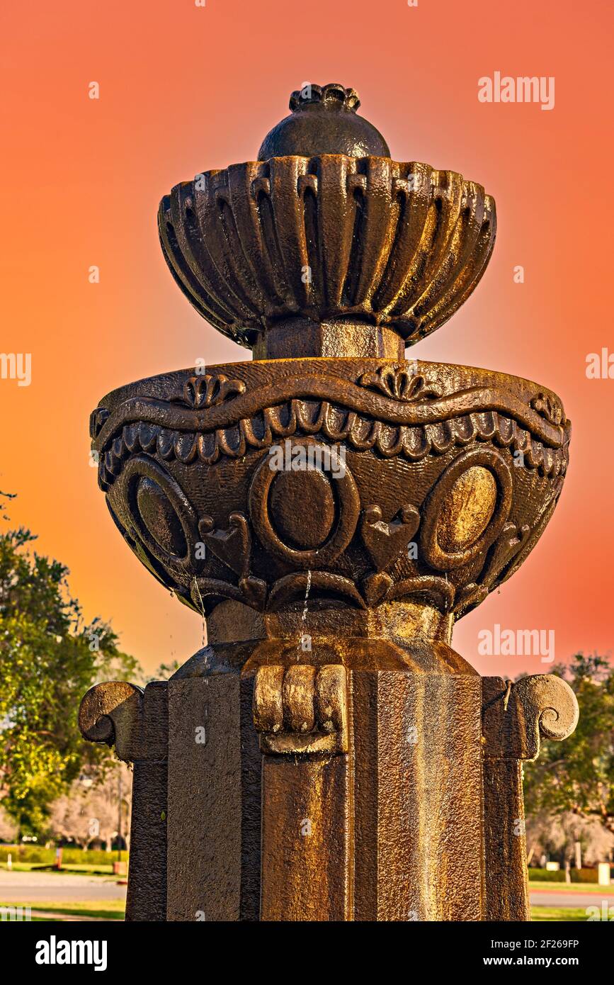 Fontana di pietra scolpita che sgocciolano l'acqua contro i cieli di tramonto arancione. Foto Stock