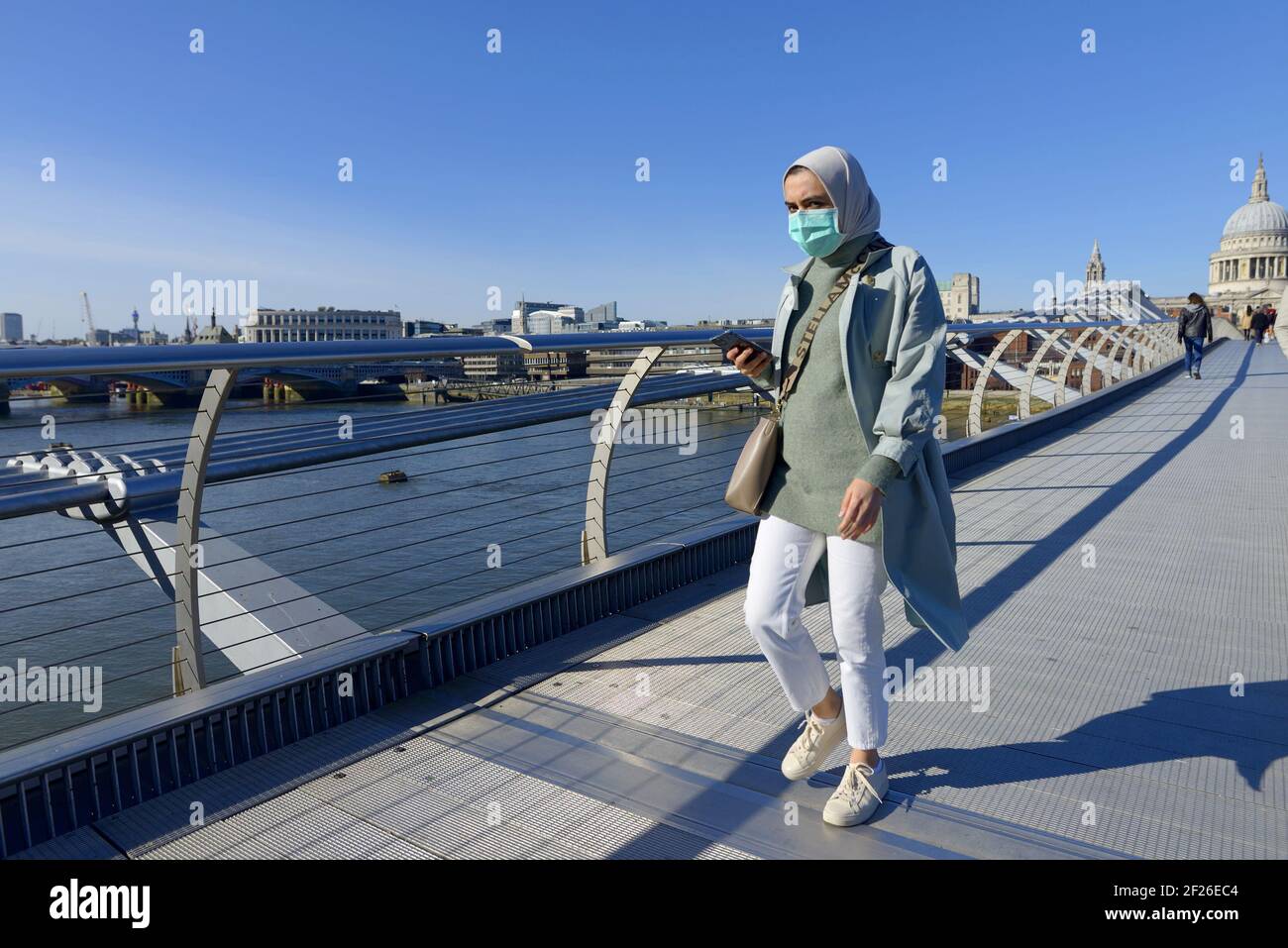 Londra, Inghilterra, Regno Unito. Mussola donna che indossa una maschera sul Millennium Bridge durante la pandemia COVID, marzo 2021 Foto Stock