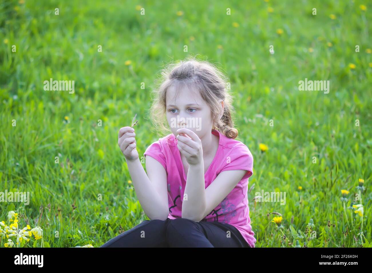 Una ragazza seduta su erba verde nel giardino primaverile. Bambini che esplorano la natura. Foto Stock