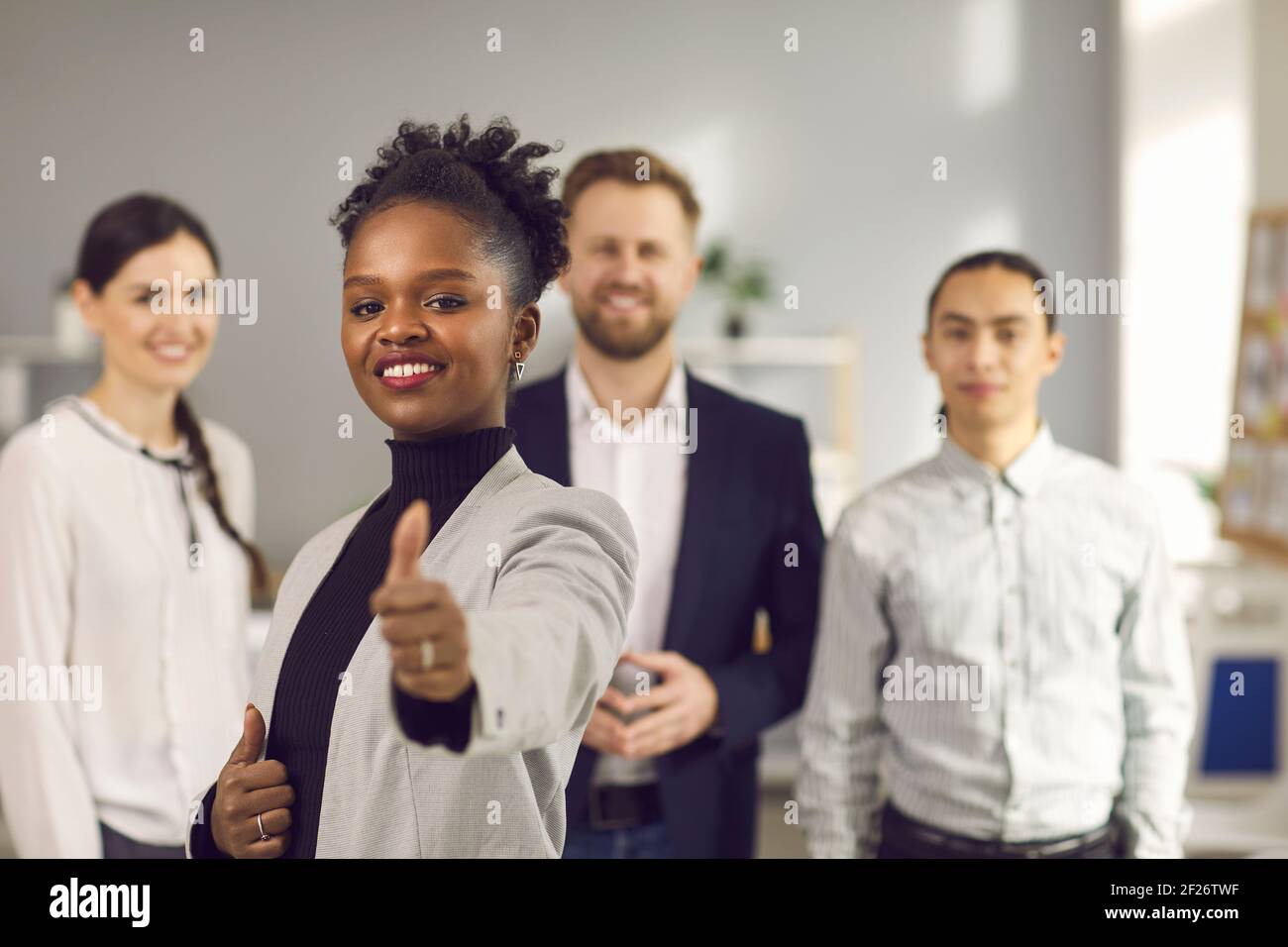 Cliente femminile che mostra il pollice in piedi sullo sfondo di una giovane squadra startup. Foto Stock