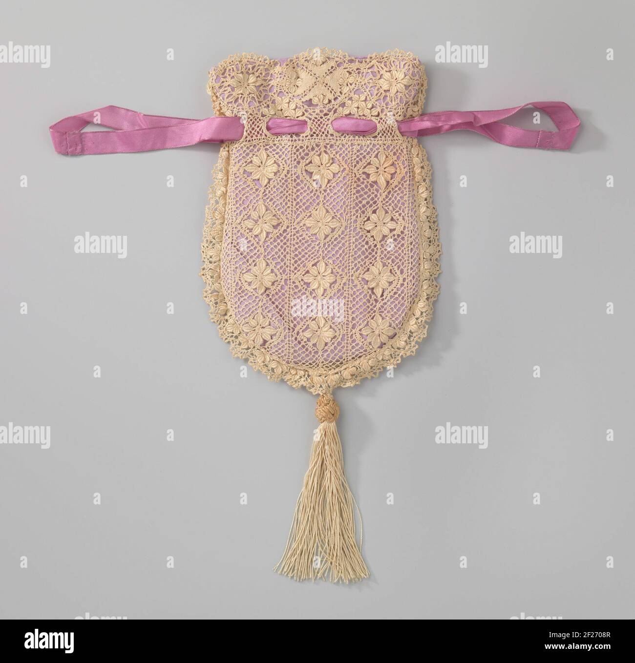 Reticule in een afgeronde vorm van ecrukleurig kant bestaande uit een patroon van twaalf rozetten aan beide zijden, onderaan een kwast.reticule in una forma arrotondata di merletto ecru-colorato costituito da un motivo di dodici rosette, ciascuna in un disegno di diamante. La parte anteriore e posteriore hanno lo stesso schema. Lungo il bordo superiore un lavoro di tre medaglioni ovali, con la metà di una croce di Malteser e quattro piccole rosette. Con aperture per una fila viola rosa slint. Sul fondo del sacchetto una spazzola. La fodera è realizzata in viola chiaro lato artificiale. Foto Stock