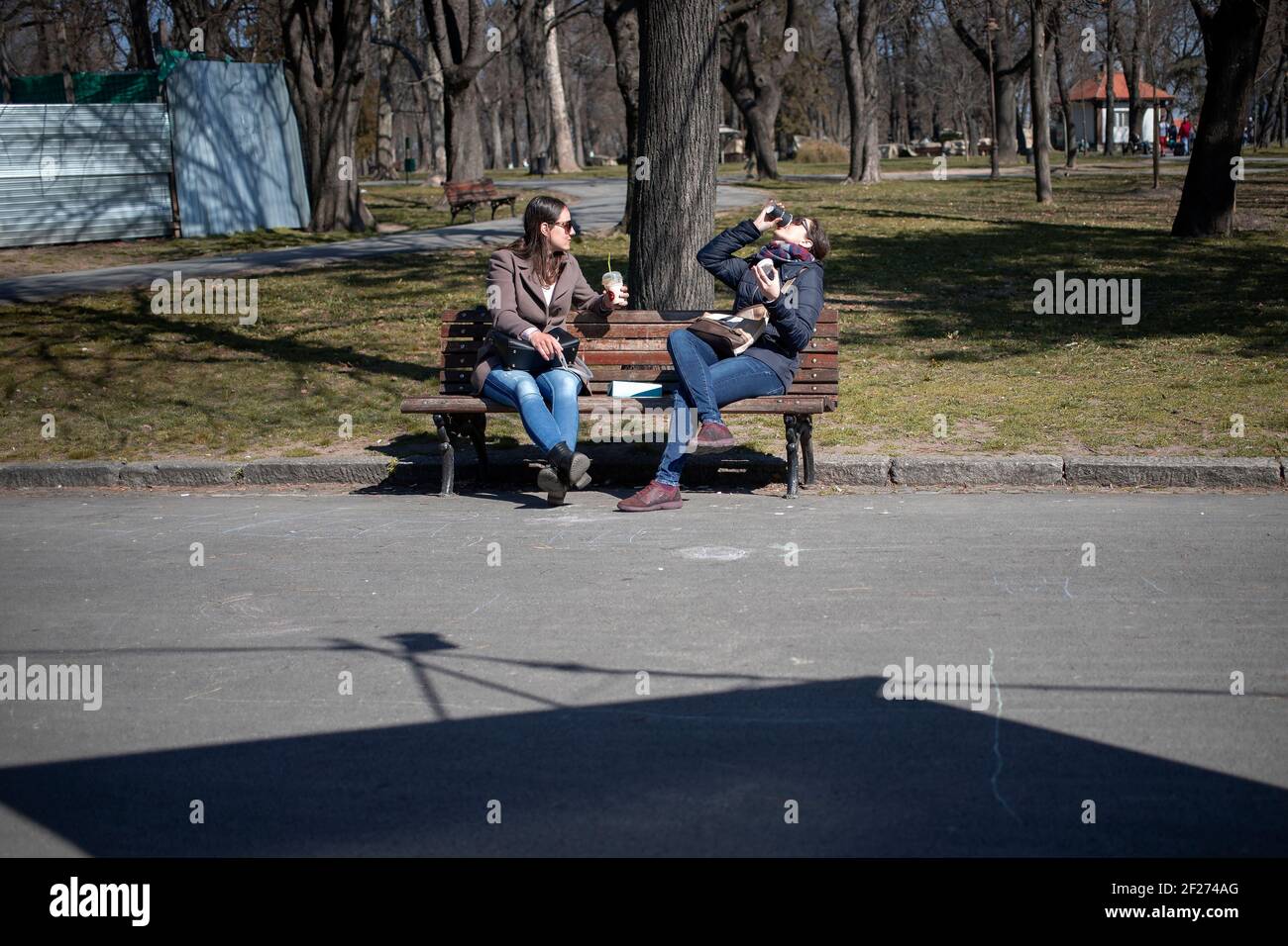Belgrado, Serbia, 7 marzo 2021: Due donne sedute su una panchina godendo di caffè e sole Foto Stock