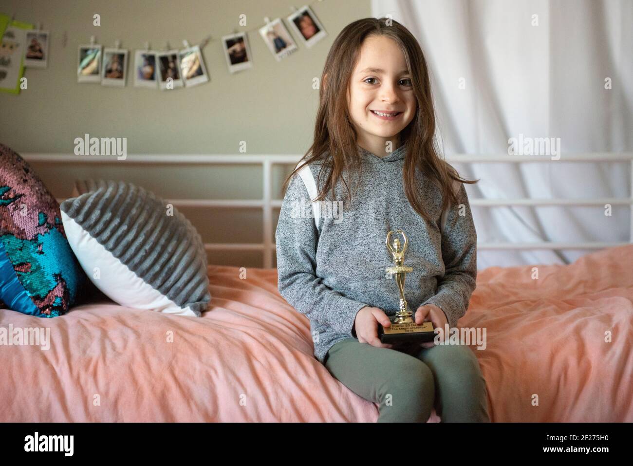 Carina bambina seduta su un letto che tiene un trofeo. Foto Stock