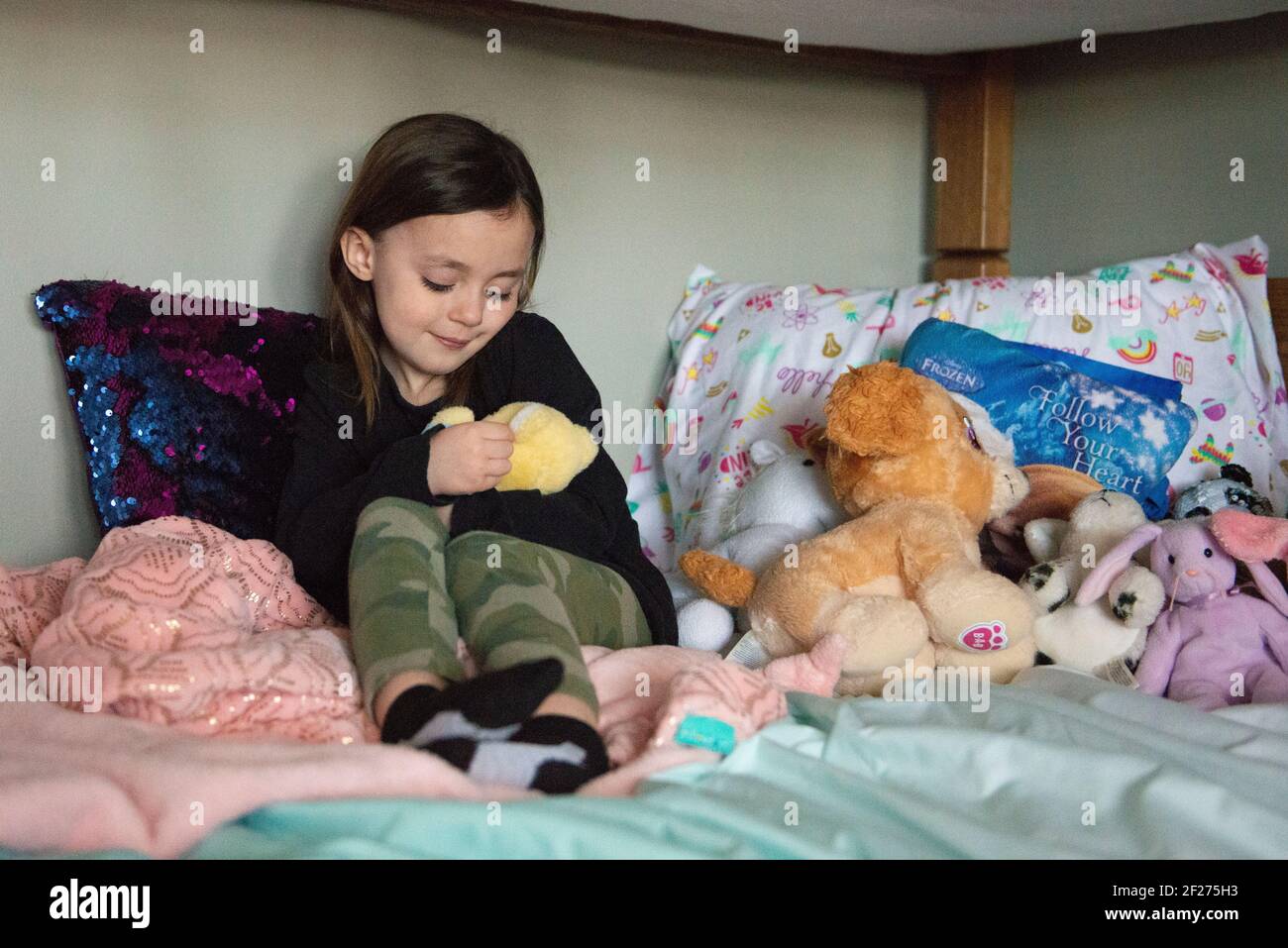 Bambina seduta su un letto con i suoi animali imbalsamati. Foto Stock