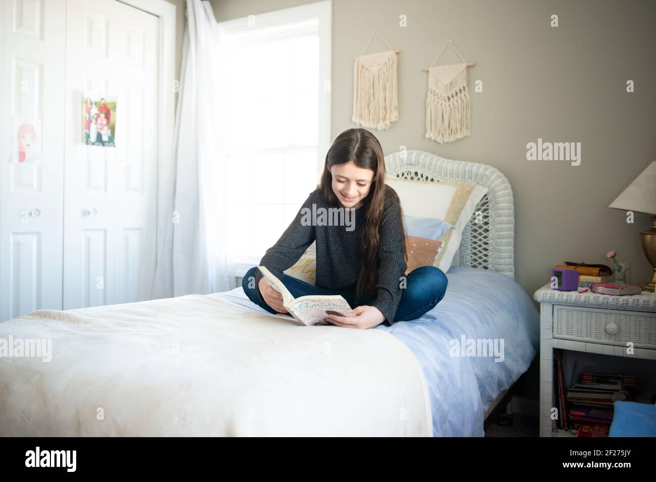 Tween ragazza seduta su un letto che legge un libro in una camera da letto soleggiata. Foto Stock