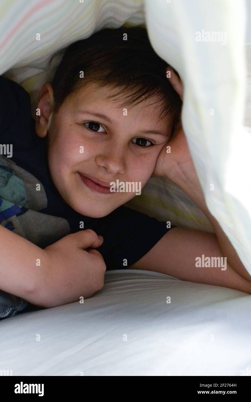 ragazzo sorridente nel suo letto sotto la coperta Foto Stock