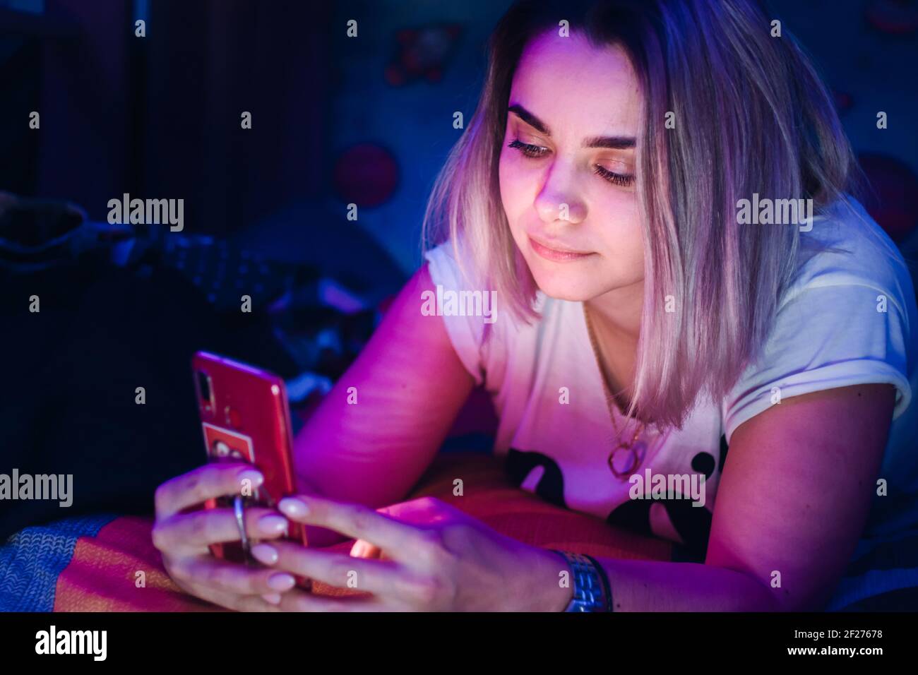 Giovane donna sdraiata a letto utilizzando il suo smartphone a casa di notte Foto Stock