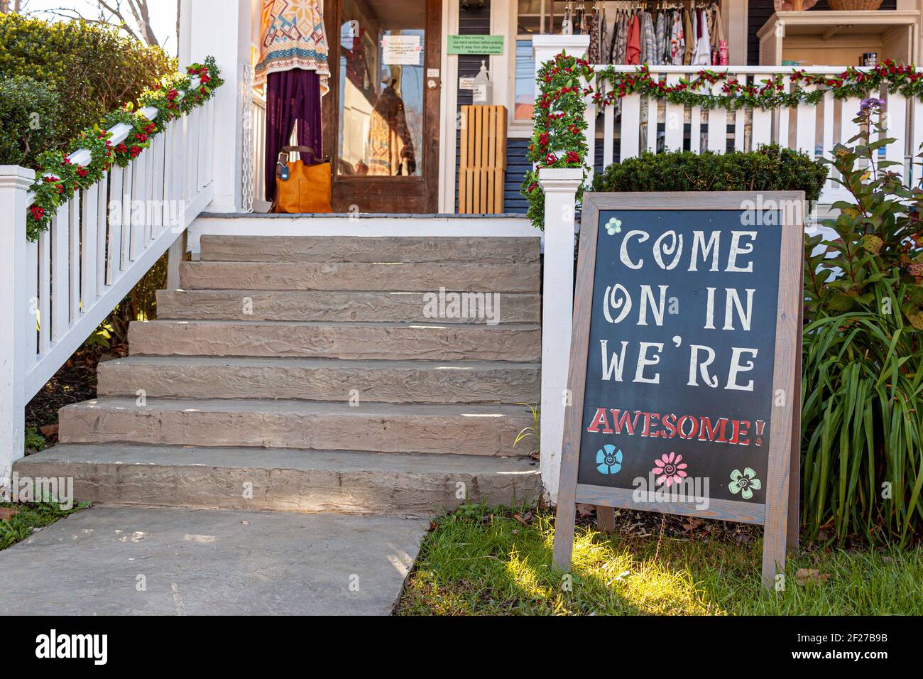 Una tavola a sandwich con un avviso di benvenuto su di essa che recita: ' come on in, we are awesome ' è collocato nel cortile anteriore di un piccolo negozio di abbigliamento locale Foto Stock