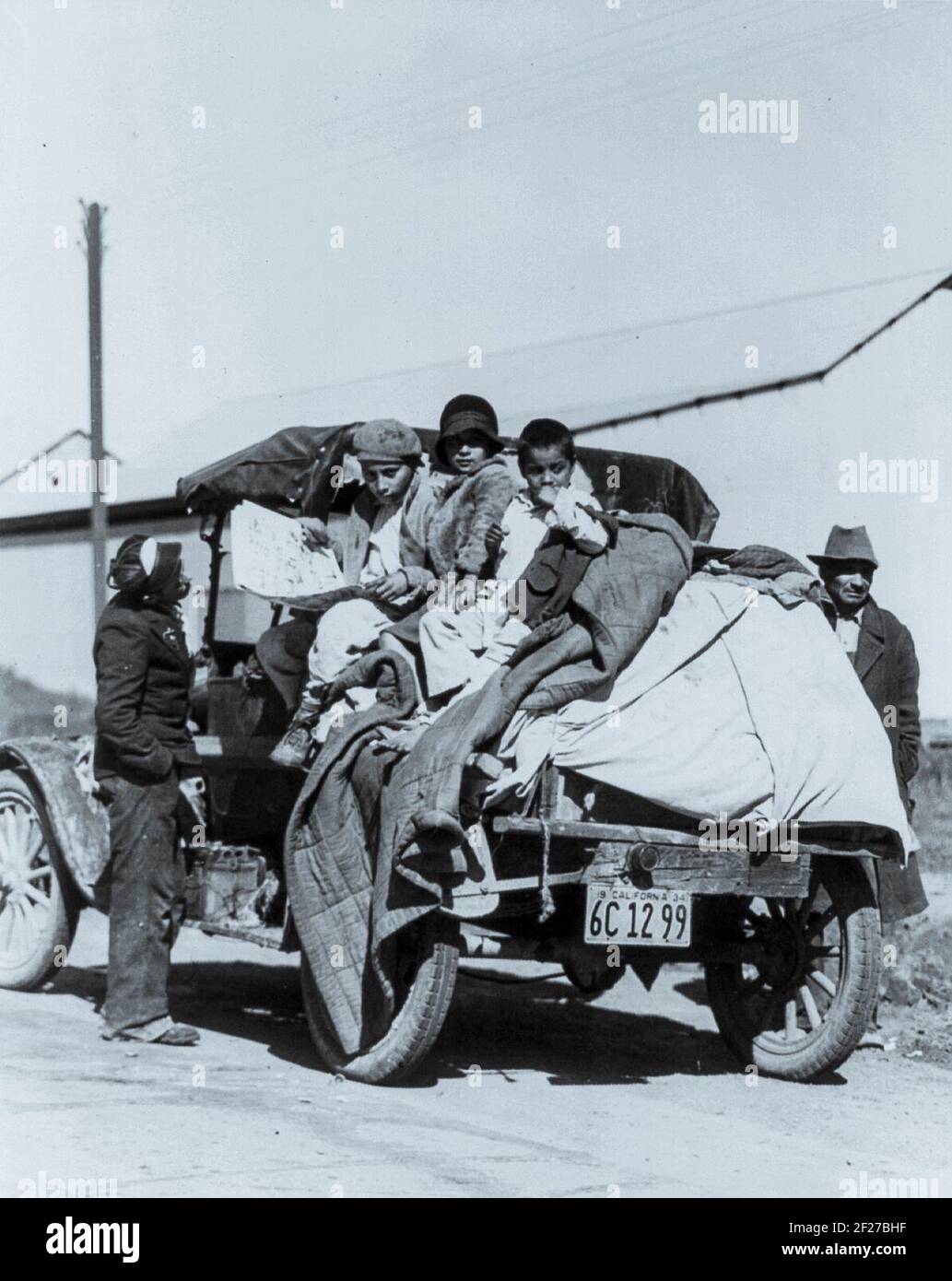 Per raccogliere i raccolti della California migliaia di famiglie vivono letteralmente su ruote, San Joaquin Valley. La fotografia mostra i bambini seduti sopra gli oggetti di famiglia accumulati sul retro di un autocarro con pianale; due uomini sono in piedi ai lati del camion. 22 febbraio 1935. Fotografia di Dorothea Lange Foto Stock