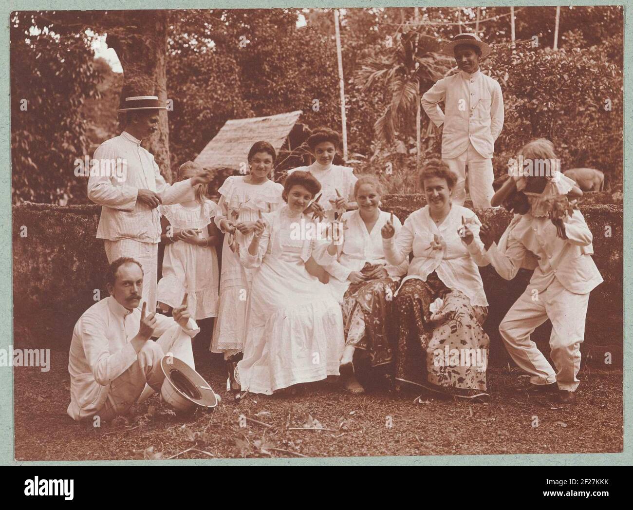 Groepsportret van jollie mensen a Batuan, gekleed in het wit.; Batoewan bij Soemenep 1910; Photographieën.gli uomini indossano uniformi tropicali bianche, un uomo con casco tropicale, altri due uomini indossano un cappello di paglia, le donne indossano abiti bianchi o gonne batik con tacchi bianchi. Foto dell'album 'Photographies'. Foto Stock