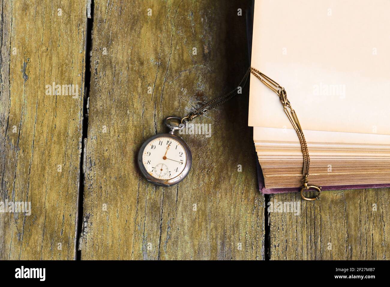 Un orologio da tasca antico e un vecchio libro su un pavimento in legno giallo Foto Stock