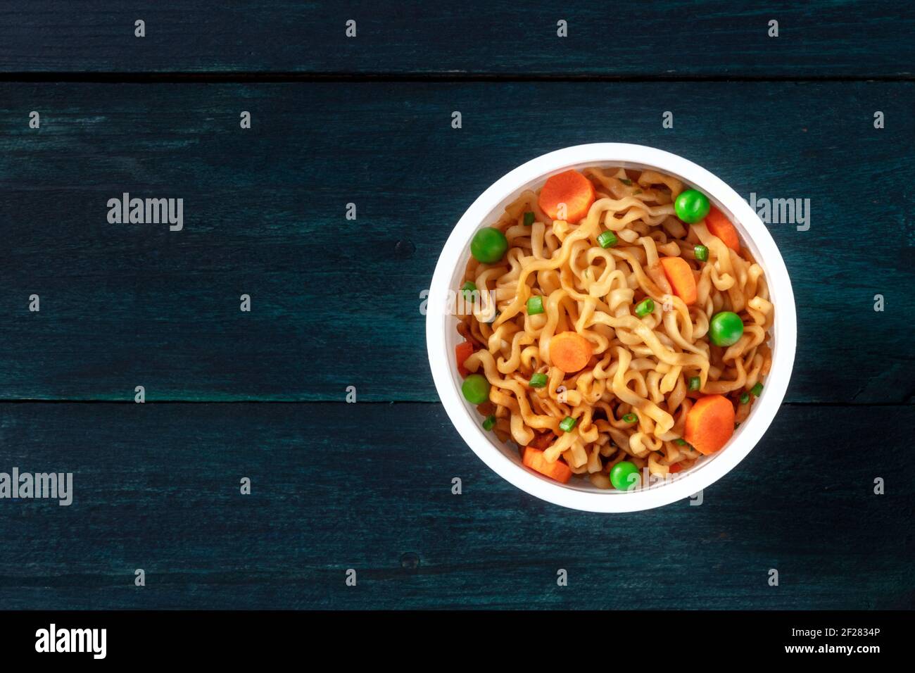 Spaghetti istantanei in una tazza di plastica, sparati dall'alto su uno sfondo blu scuro Foto Stock