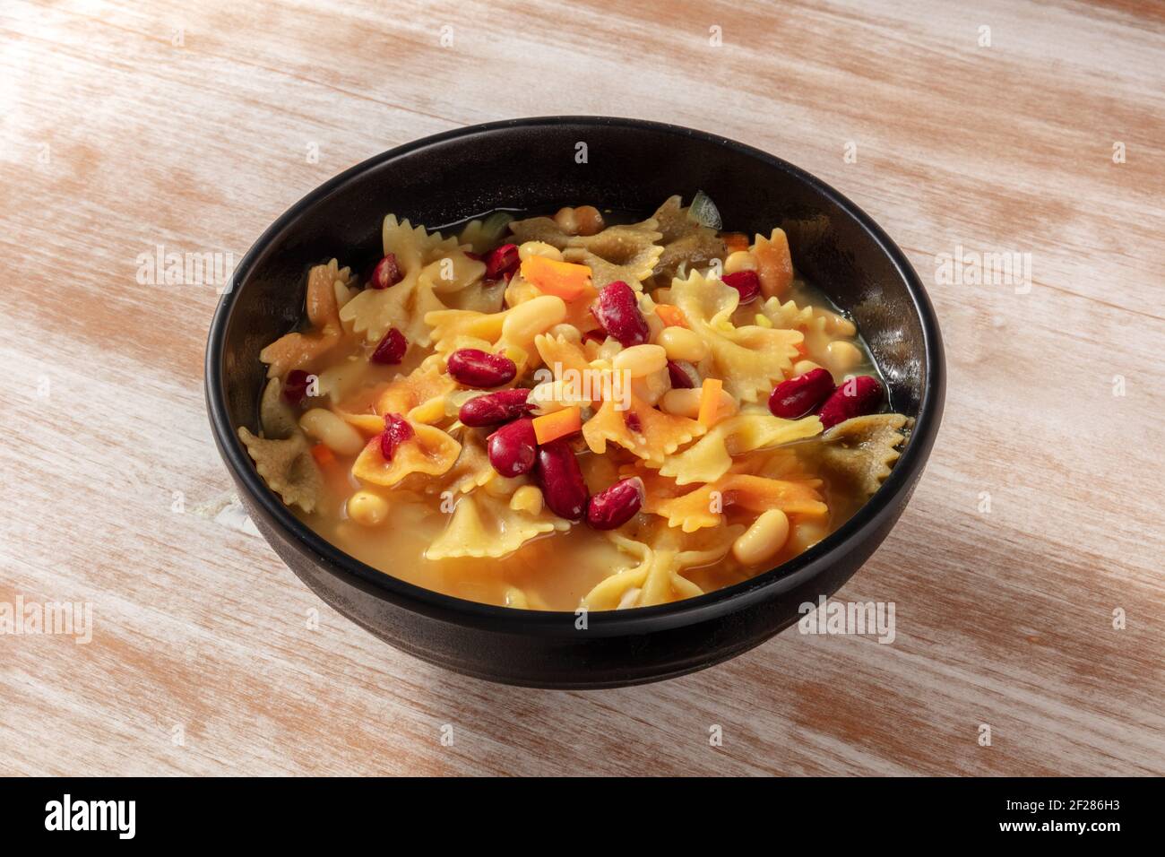 Zuppa vegana con verdure, pasta e fagioli, su sfondo rustico Foto Stock