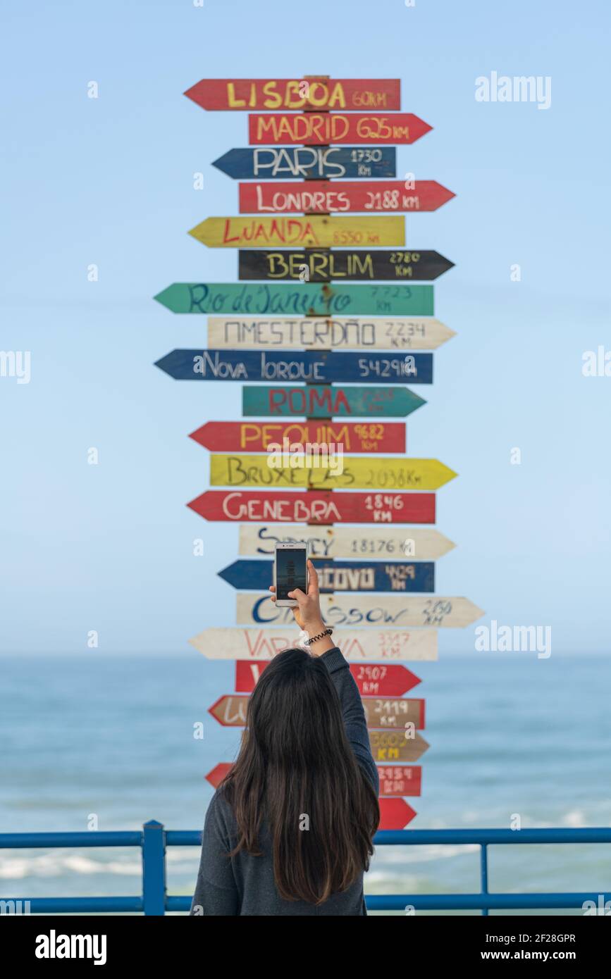 Donna viaggiatore fotografando frecce di indicazione per le città di tutto il mondo a Torres Vedras, Portogallo Foto Stock