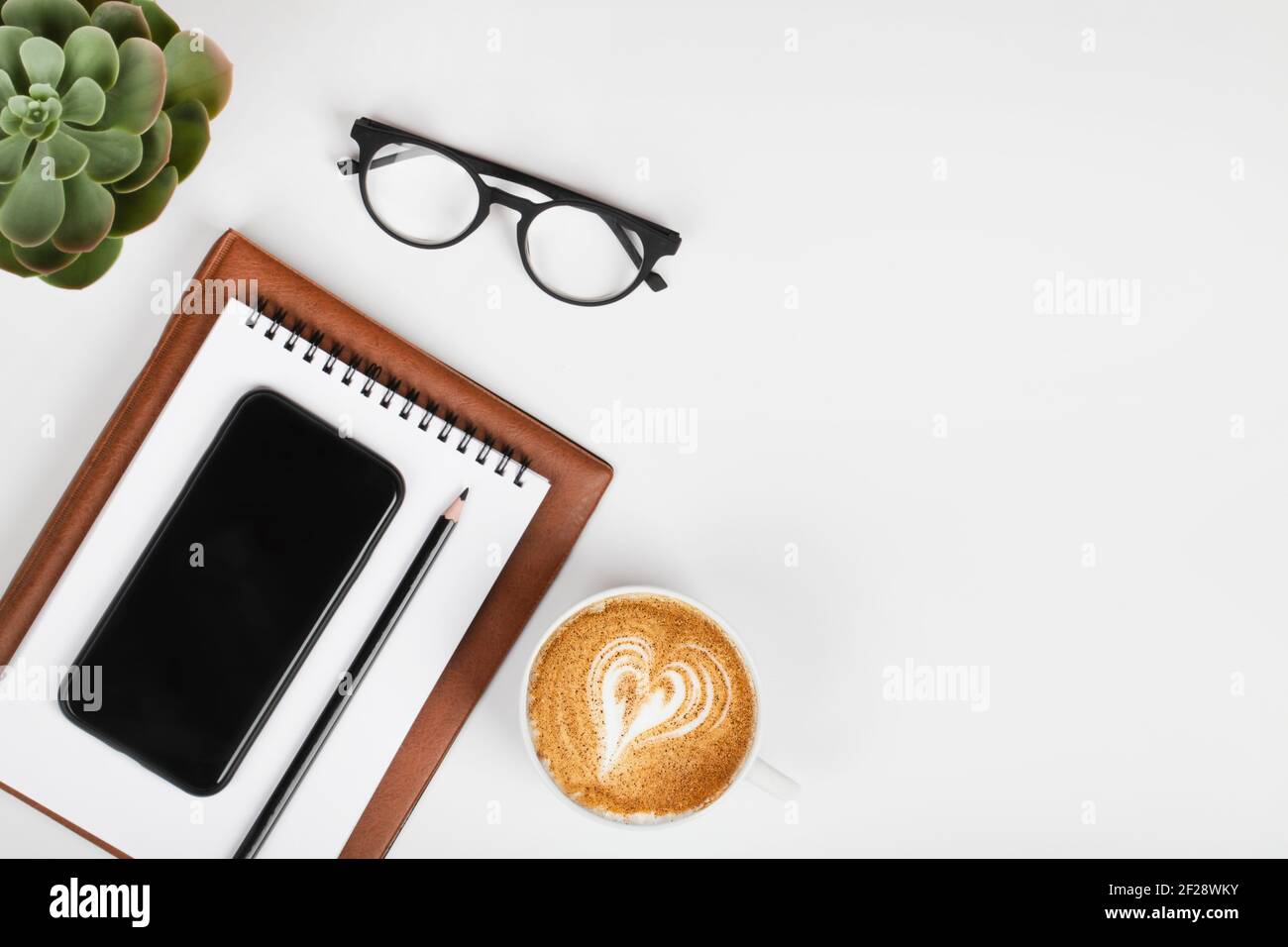 scrivania da tavolo per ufficio, area di lavoro con telefono cellulare, notebook, matita, piante verdi, caffè e occhiali. Background aziendale. Disposizione piatta, spazio di visualizzazione superiore.copia Foto Stock