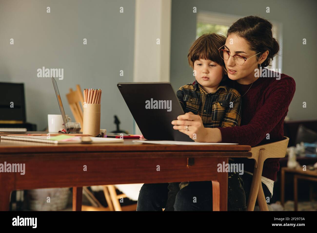 Donna e figlio seduti al tavolo utilizzando un tablet digitale. Madre che usa il tablet digitale con il figlio homeschooling. Foto Stock