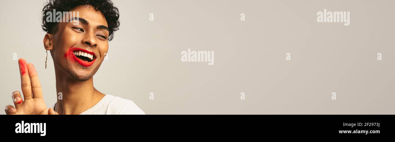 Uomo gay sorridente con rossetto sbavato su sfondo bianco panoramico uomo con rossetto sbavato sul viso guardando via lo spazio della copia. Foto Stock