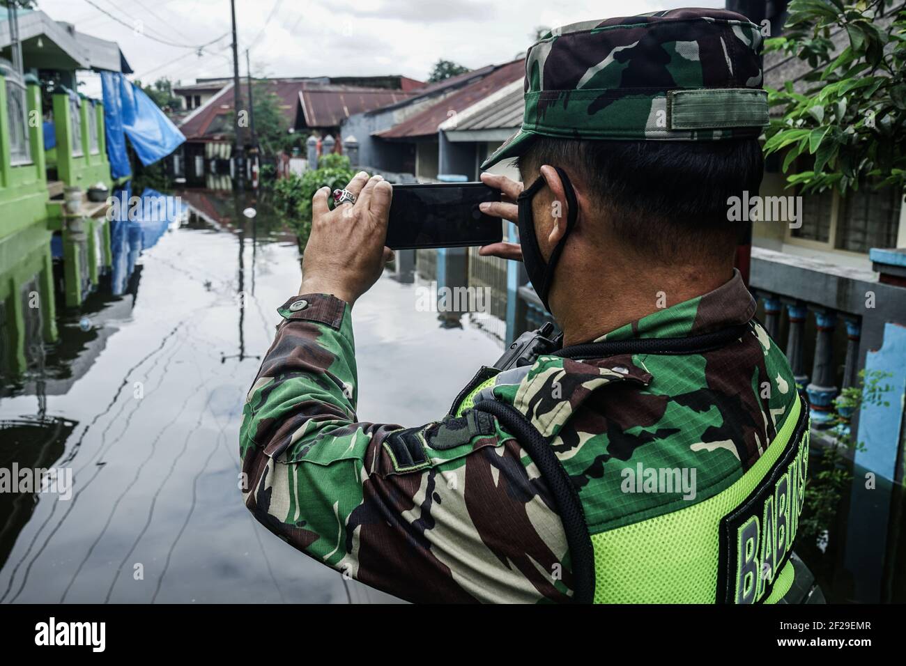 Makassar, Sulawesi del Sud, Indonesia. 11 Marzo 2021. Un soldato sta scattando foto di un certo numero di case colpite dall'alluvione usando un telefono cellulare. Le inondazioni si sono verificate nella città di Makassar e hanno causato l'immersione di decine di case in acqua, in modo che i residenti dovevano essere evacuati in un luogo più sicuro. Credit: Herwin Bahar/ZUMA Wire/Alamy Live News Foto Stock