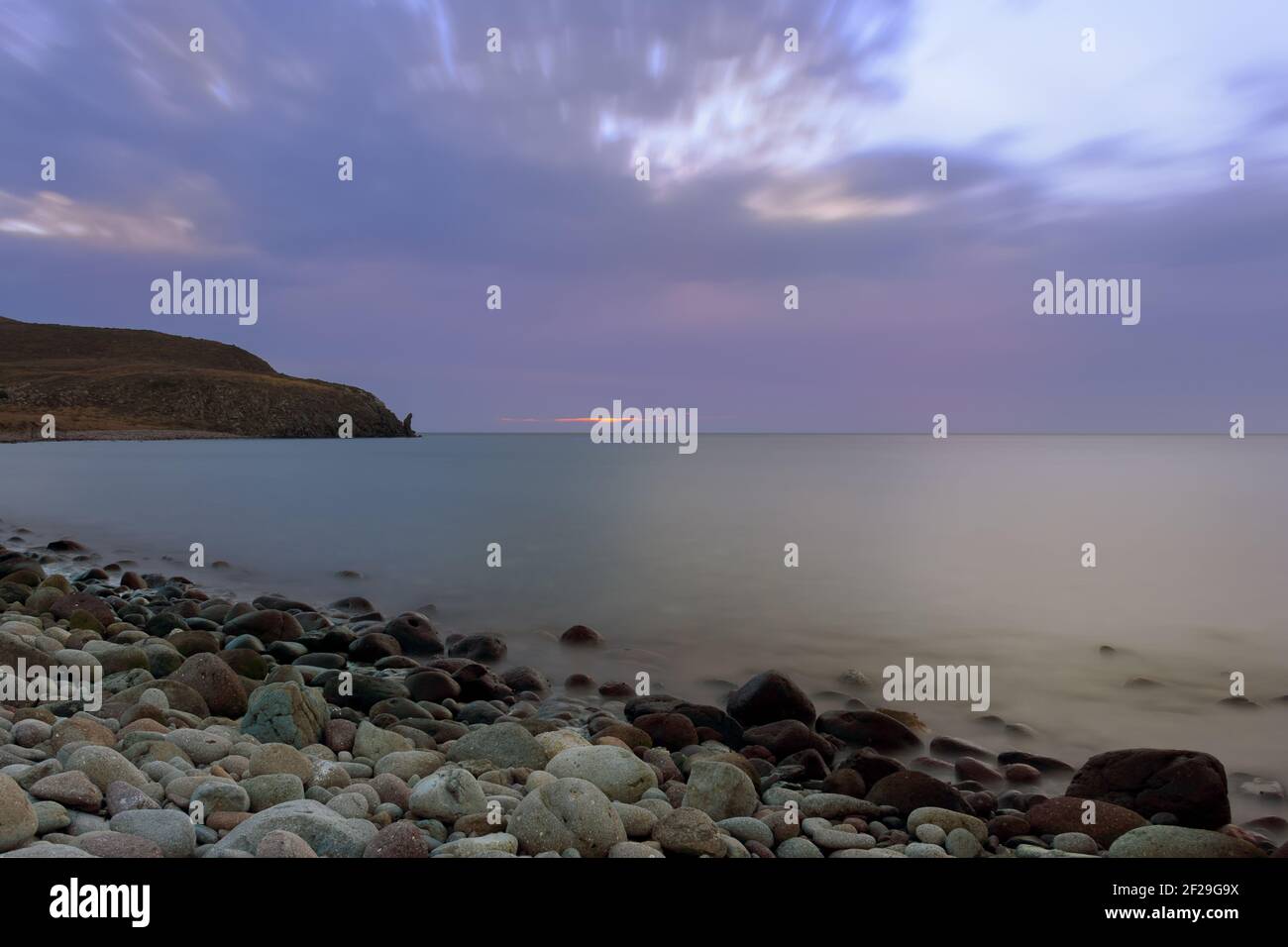 Spiaggia a lunga esposizione con pietre al tramonto, con cielo nuvoloso Foto Stock