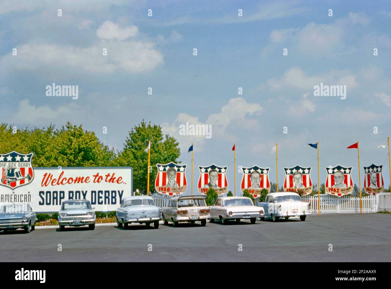 Il parcheggio presso Derby Downs, Akron, Ohio, USA nel 1964. Il locale è stato il circuito di casa del ‘All American SOAP Box Derby’ da quando è stato costruito come progetto di Works Progress Administration (WPA) negli anni trenta. Le tradizioni abbondano con un cartello di benvenuto e famosi vincitori precedenti di gare mostrate su striscioni, tra cui James Miley (1958) e David Mann (1962). La pista asfaltata a tre corsie inizia vicino alla cima del George Washington Boulevard e scende in linea retta lungo la collina boscosa. Questa immagine è tratta da un vecchio lucido a colori americano amatoriale Kodak – una fotografia d'epoca degli anni '60. Foto Stock