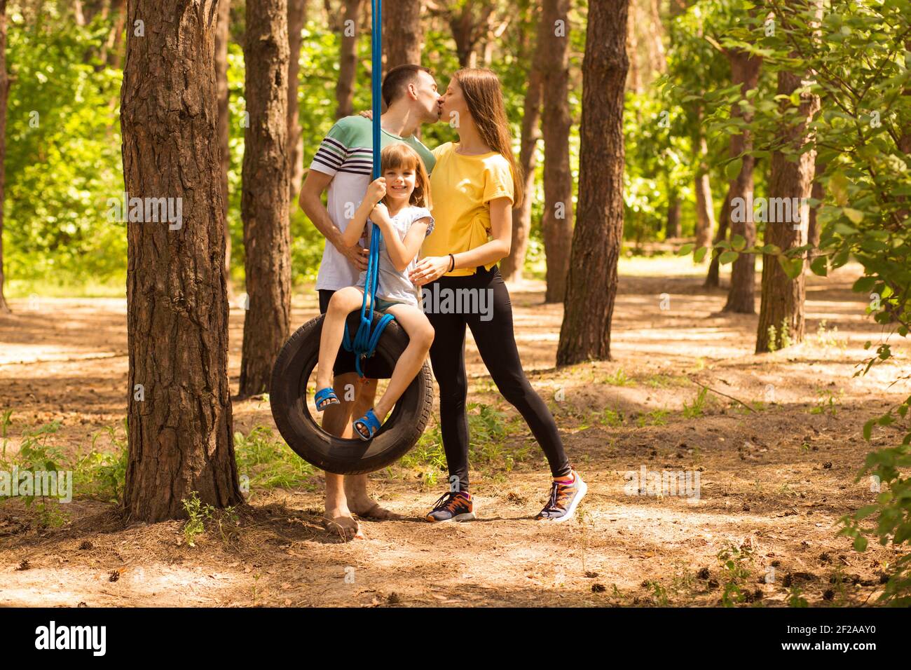 Bella giovane genitore felice che swing figlia felice su ruota, in estate natura sullo sfondo, tempo attivo insieme Foto Stock