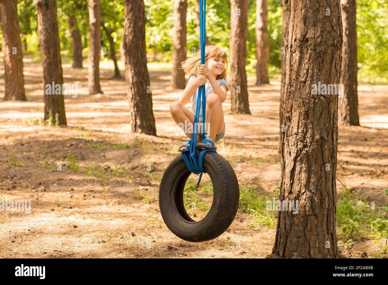 Carino bambina che oscilla sulla ruota attaccata al grande albero nella foresta di autunno. Foto Stock