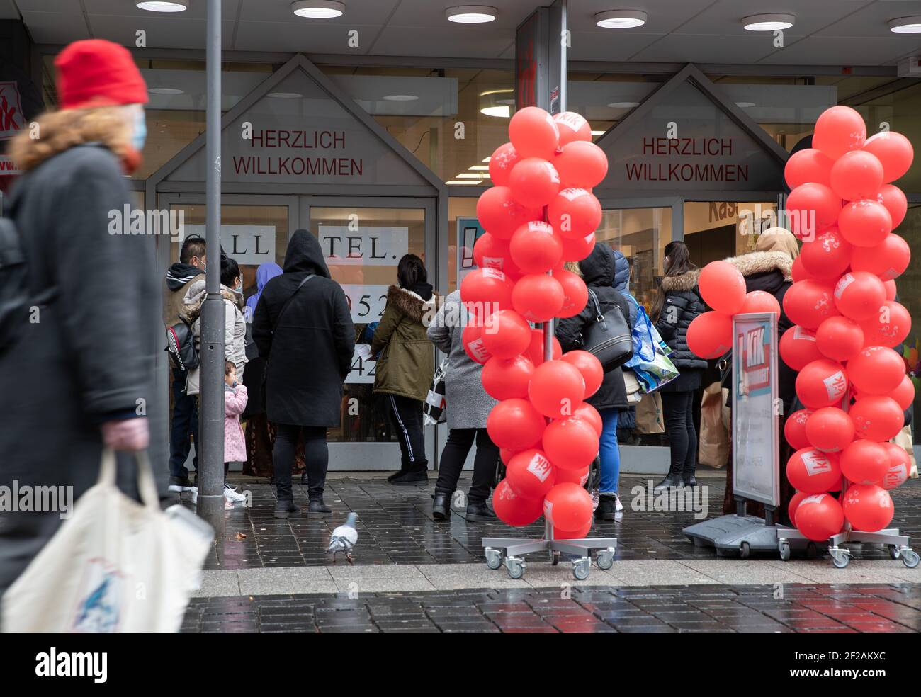 Bielefeld, Germania. 11 Marzo 2021. I clienti si accodano di fronte a un negozio decorato con palloncini nella zona pedonale. Diversi comuni della NRW con bassi numeri di corona stanno approfittando dell'opportunità di relax locale nel commercio e nella cultura e di offrire sprees shopping senza registrazione. Credit: Friso Gentsch/dpa/Alamy Live News Foto Stock