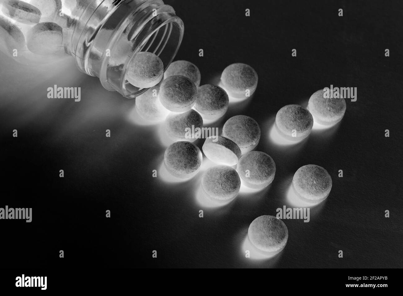 Pillole e compresse fuoriescono dal flacone di vetro per pillola su sfondo nero lucido misterioso Foto Stock