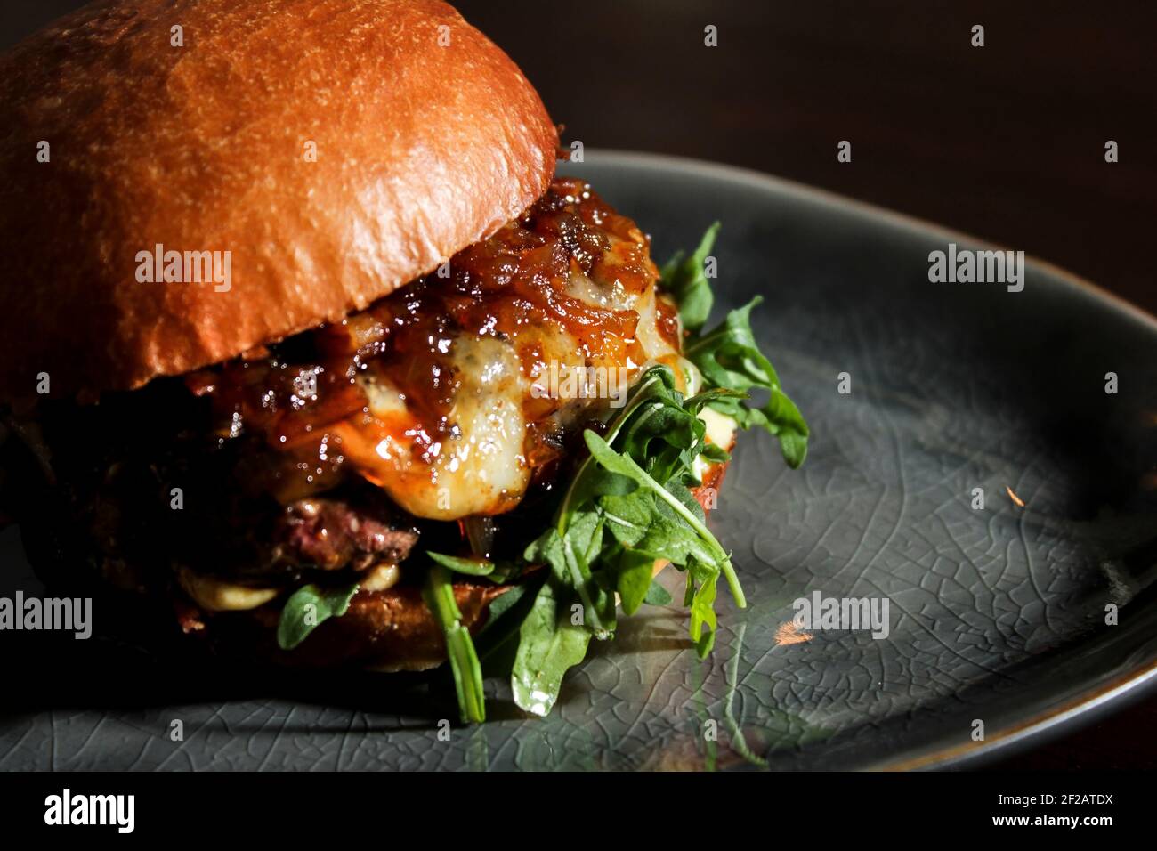 Succulento hamburger di manzo con cipolla caramellata, formaggio e rucola su panna fatta in casa. Foto Stock