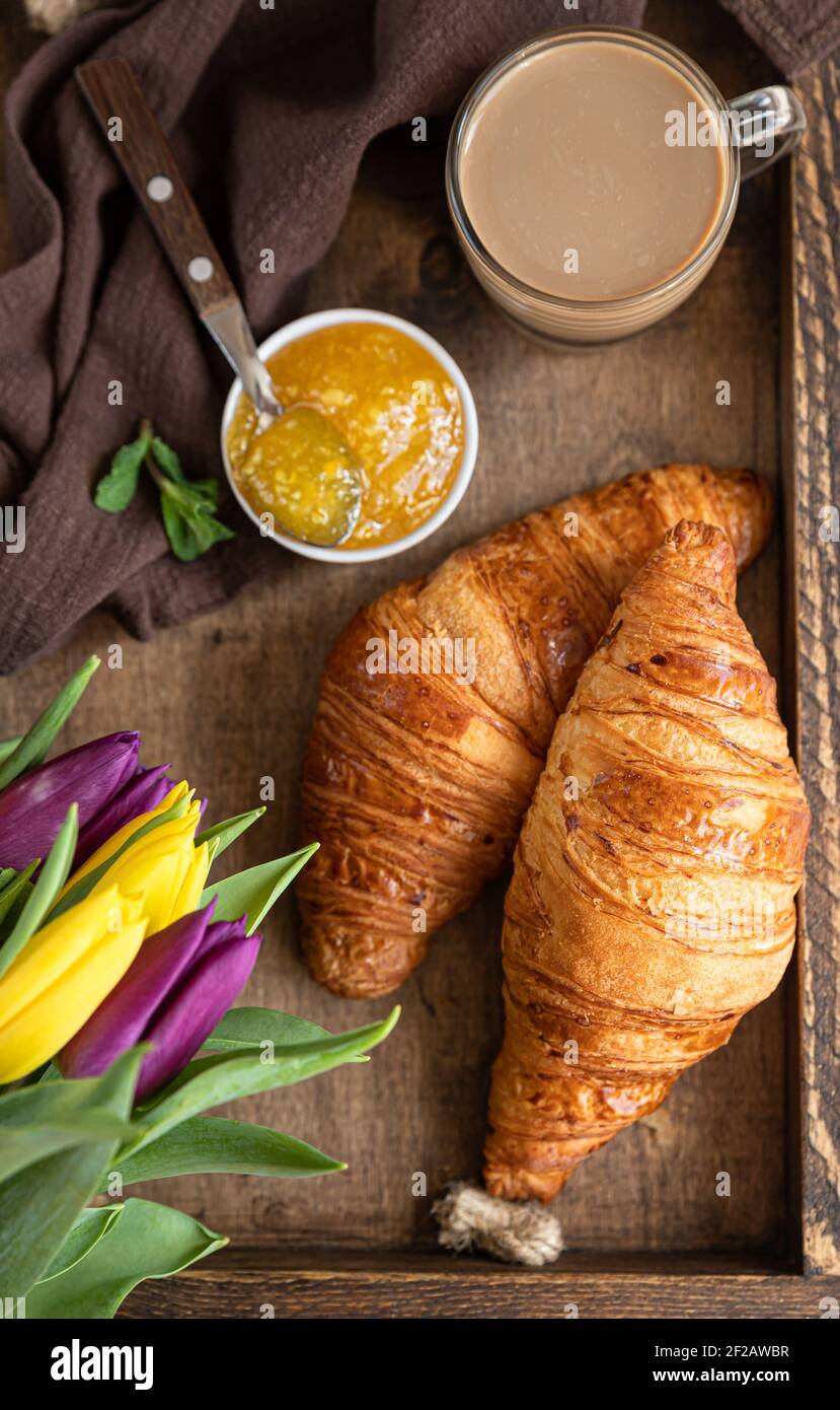 Colazione romantica con croissant croccanti, marmellata, crema di cioccolato, caffè e tulipani colorati su vecchio vassoio di legno fuoco selettivo. Foto Stock