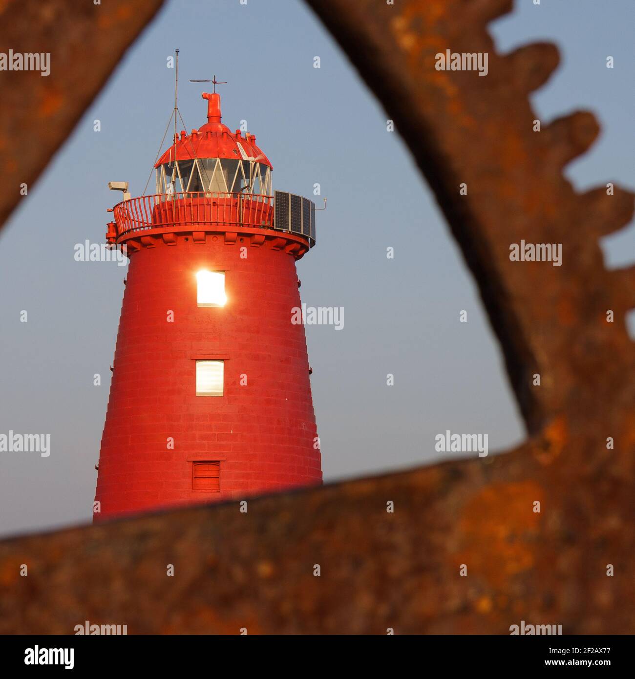 Faro di Poolbeg visto attraverso l'attrezzatura e la ruota di gru portuale, faro rosso, porto di Dublino, attrezzatura arrugginita, vecchia gru manuale, cielo blu, quadrato, Foto Stock