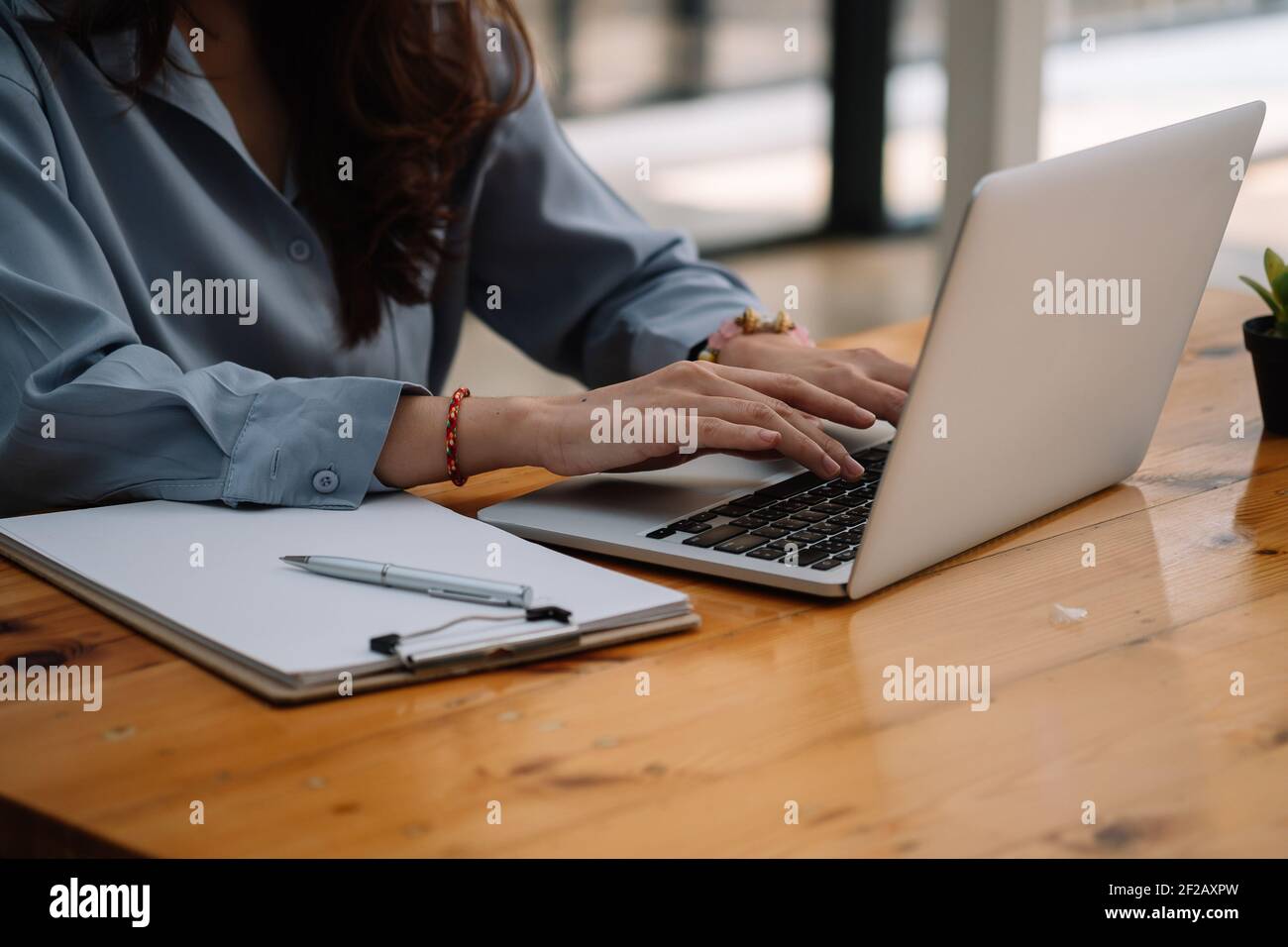 Primo piano delle mani della ragazza studentesca che mettono a confronto le note sul computer portatile seduto su una scrivania a casa. Foto Stock