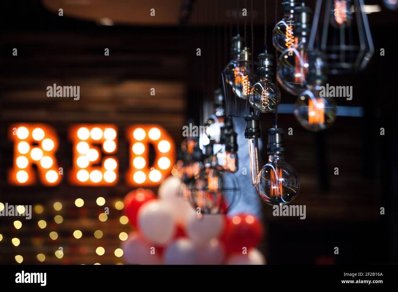 Interni scuri con molte lampade a LED ed elementi decorativi di illuminazione sotto forma di 'Rosso'. Palloncini rossi e bianchi. Foto Stock