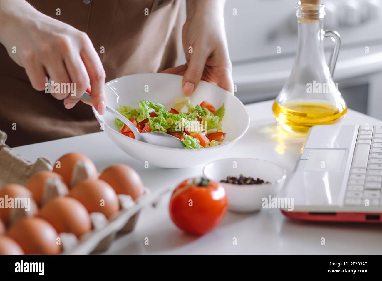 Donna che prepara l'insalata di dieta usando il libro di cucina digitale. Verdure fresche e computer portatile in cucina. Cucina online. Registra le ricette sulla fotocamera. Foto Stock