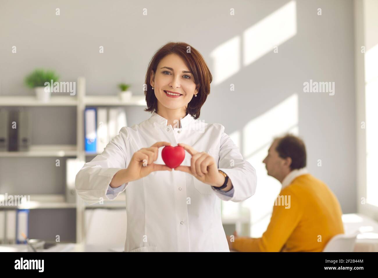 Cardiologa femminile che tiene un piccolo cuore rosso come simbolo di un importante organo umano sano. Foto Stock