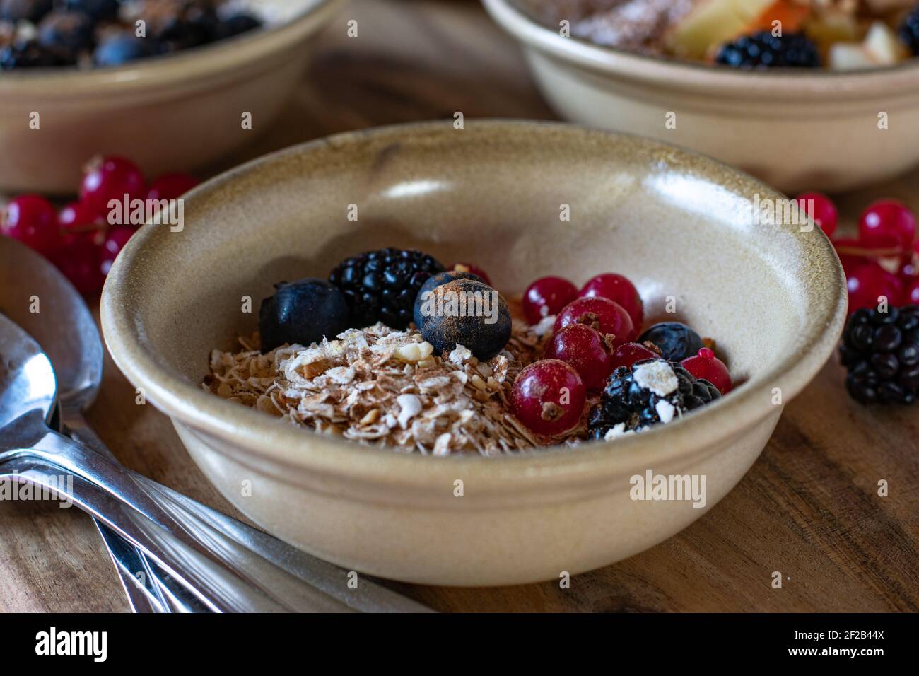 Una ciotola con farinata d'avena, noci tostate e bacche servita su un tavolo rustico per la colazione Foto Stock