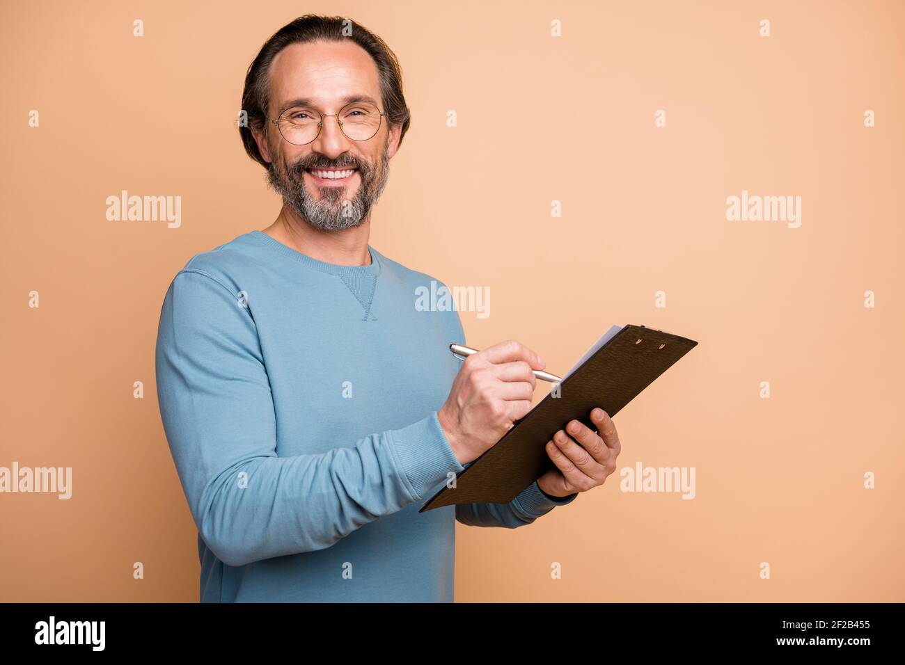 Ritratto fotografico di uomo che scrive note sulla clipboard isolato su sfondo color beige pastello Foto Stock