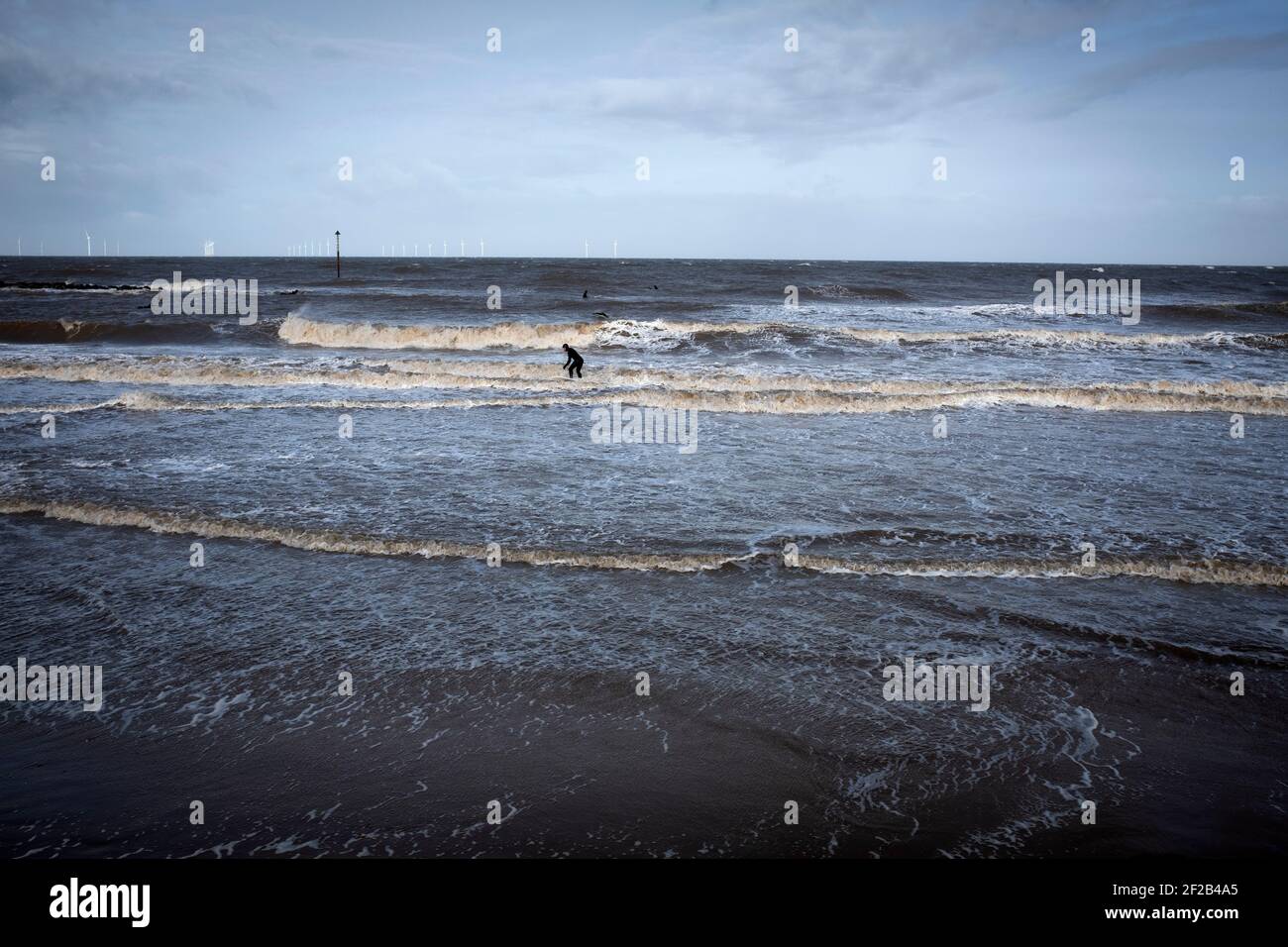 Un surfista in mare alla foce del fiume Mersey. Alte maree e una tempesta che ha attraversato il Regno Unito hanno portato le condizioni favorevoli per il surf a Leasowe Bay, Merseyside il 11 marzo 2021. Foto Stock