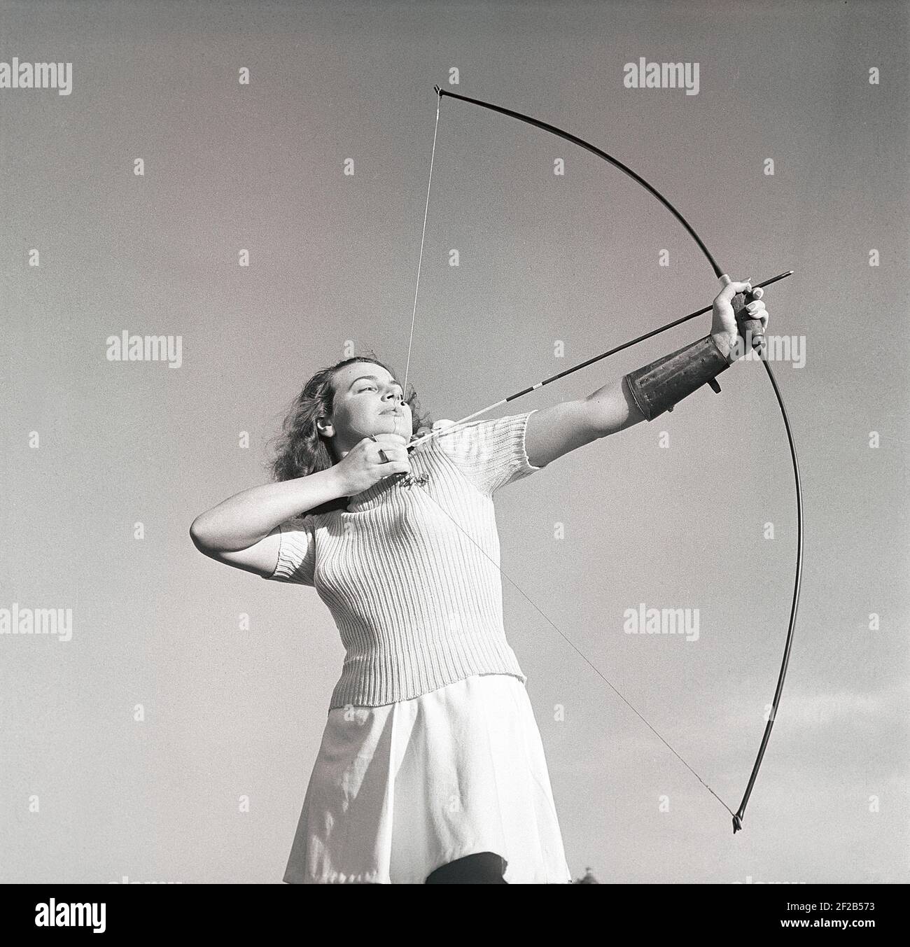 Tiro con l'arco negli anni '40. La giovane attrice svedese Mimi Nelson con un arco e una freccia, che punta a qualcosa di pronto a scattare il colpo. È vestita con il tipico jumper degli anni '40 e una gonna. Svezia 1947 Rif AD7-3 Foto Stock