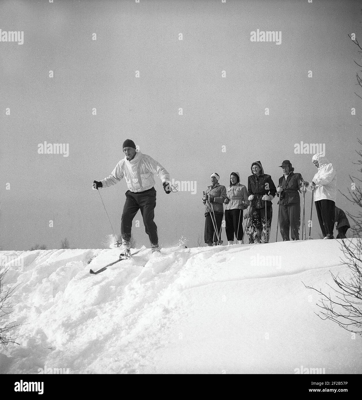 Inverno negli anni '40. Un gruppo di persone che sciano e prima di provare a sciare giù per la collina, si levano in piedi e osservano come va quando un uomo prova il suo meglio ad esso senza cadere nella neve profonda. Svezia 1947. Rif. Kristoffersson A30-9 Foto Stock