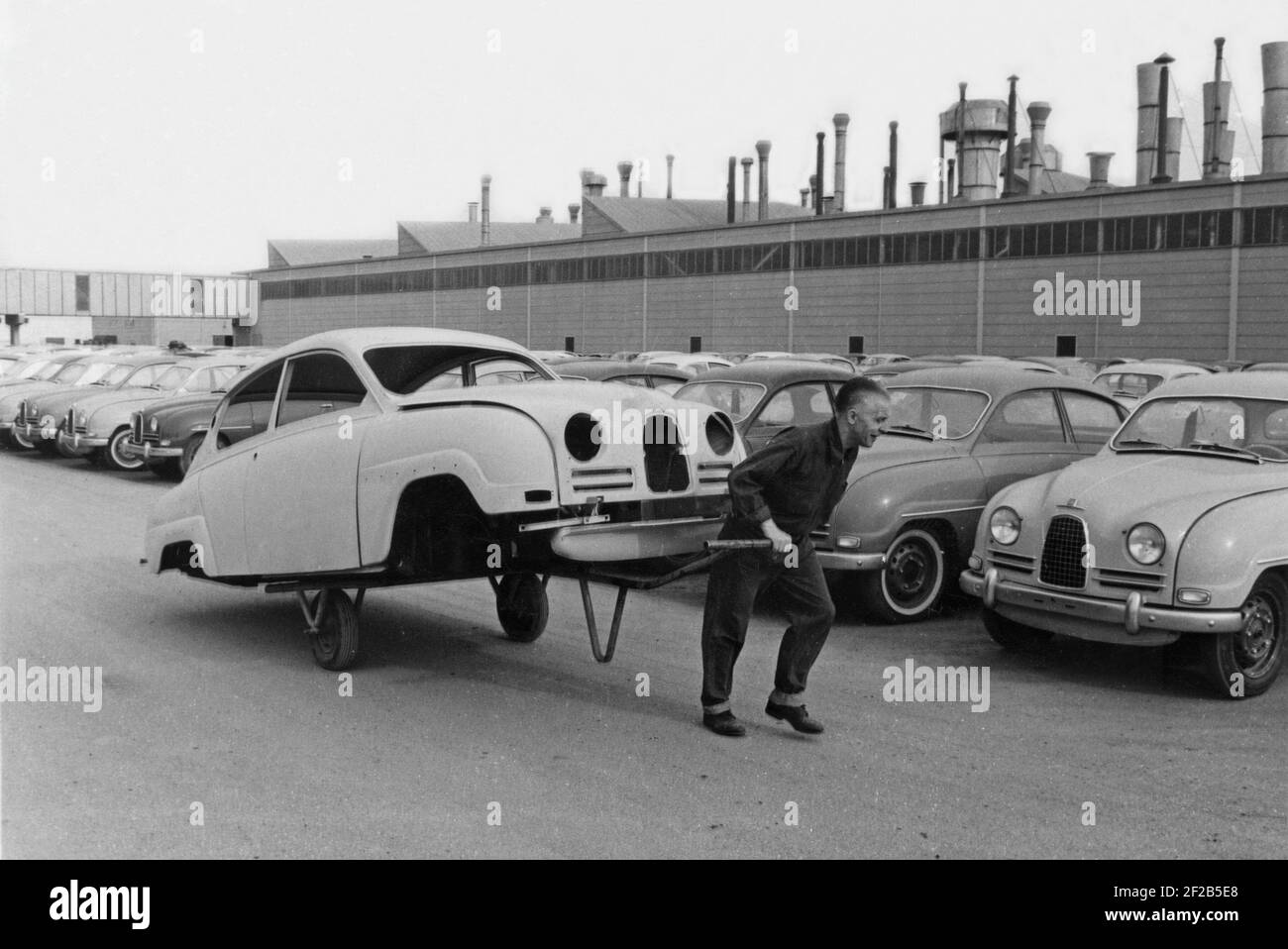 Produzione di automobili negli anni '50. La fabbrica di automobili Saab in Trollhättan Svezia con la sua linea di produzione. Una strana immagine di un lavoratore che trascina i chassi di un'automobile di Saab dietro di lui su una carrozza. Il modello è Saab 96, prodotto tra il 1960 e il 1963. Svezia 1961 Foto Stock
