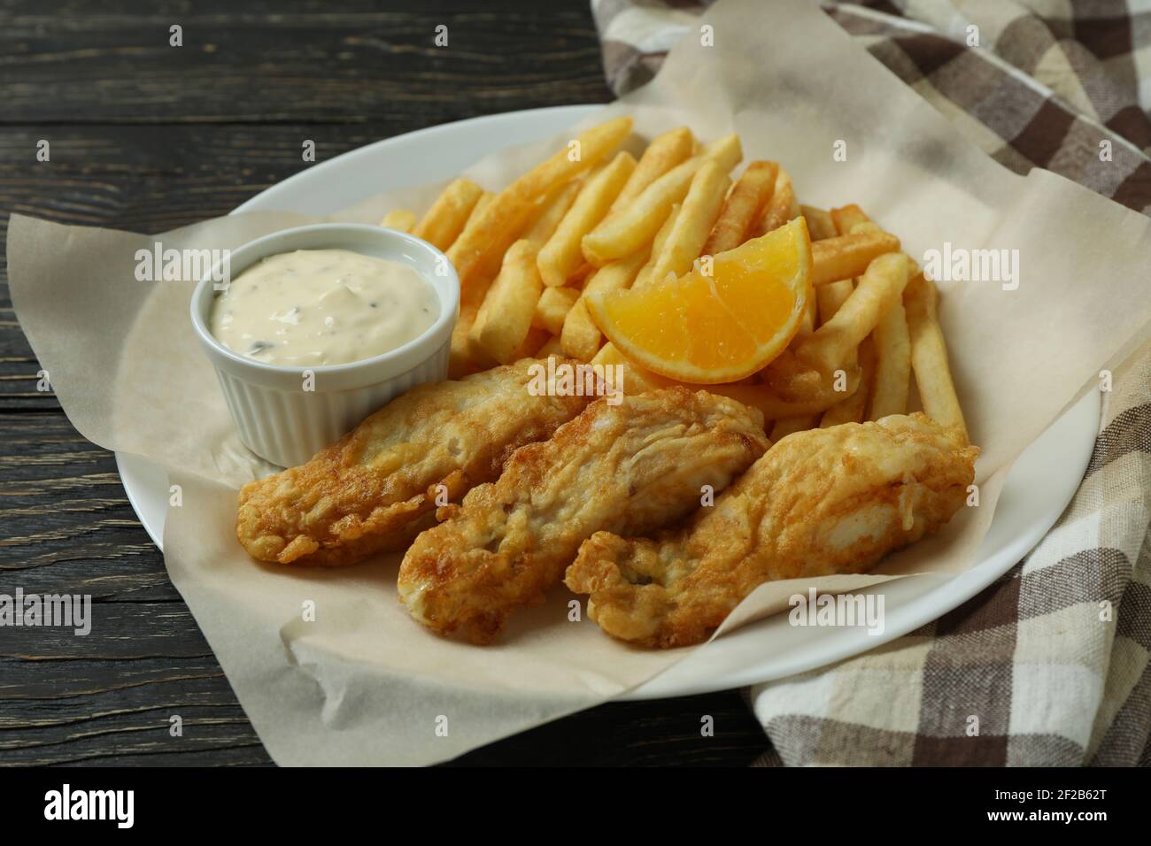 Piatto con pesce fritto e patatine su uno sfondo di legno con un canovaccio, pasto da pub fatto in casa Foto Stock