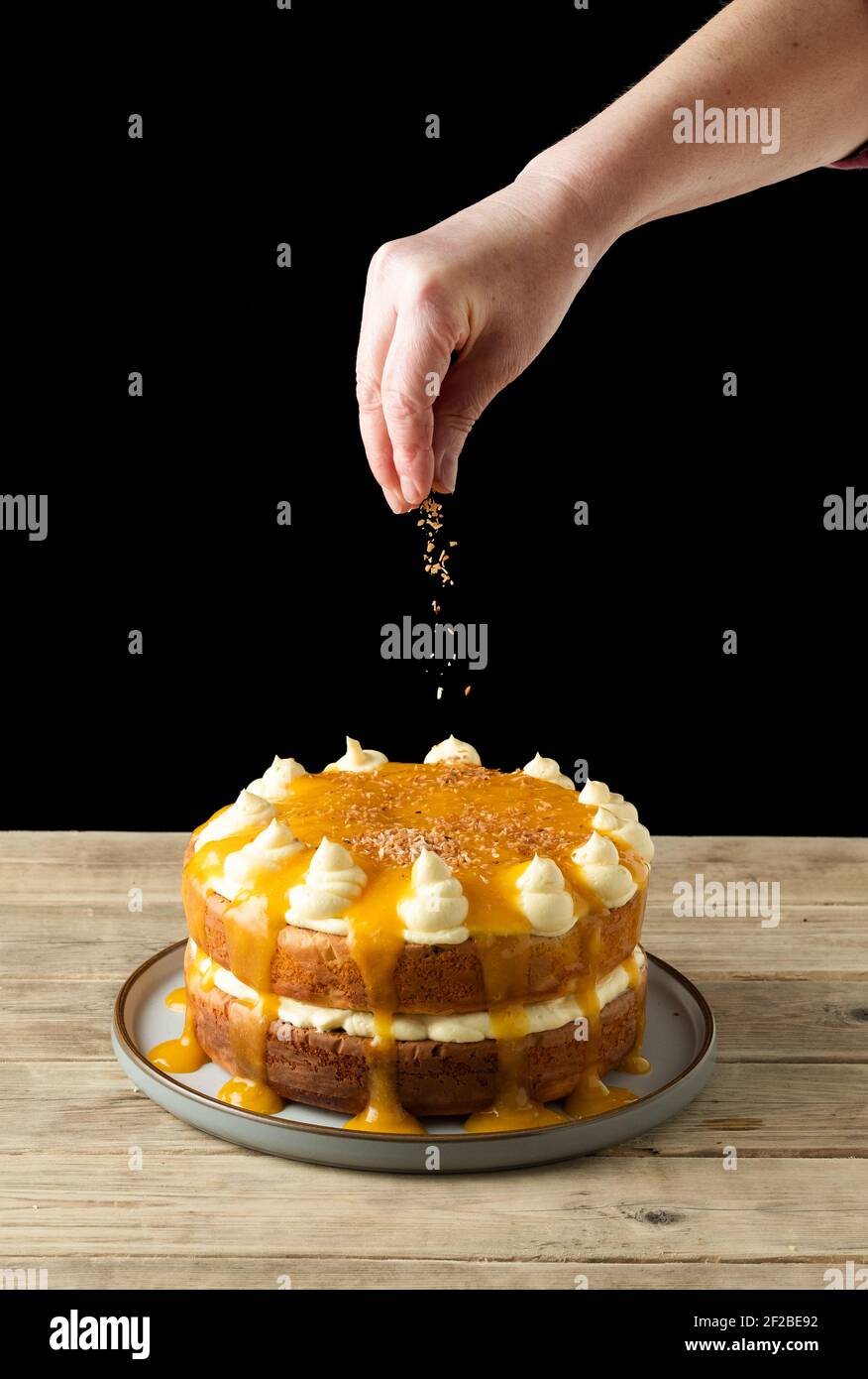 Una festa Mango, cocco e torta di yogurt. È composto da una ricetta di cottura Nadiya Hussain. Il panettiere è il cocco spruzzando sopra la parte superiore della torta Foto Stock