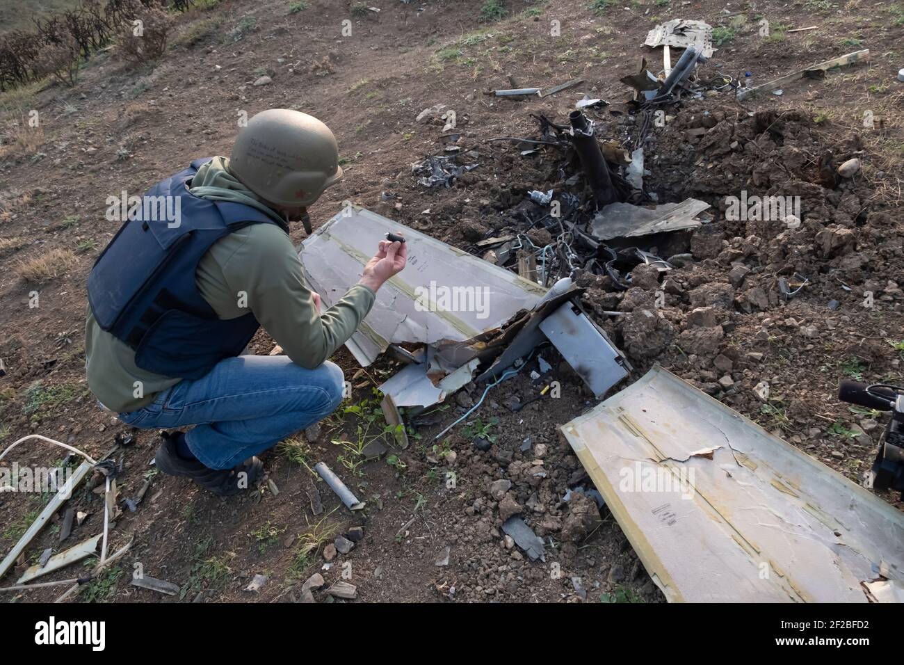 SHUSHI, NAGORNO KARABAKH - NOVEMBRE 03: Un uomo armeno che indossa una giacca e un casco di protezione in flak ispeziona i resti di un Israele depresso fatto Harop, drone kamikaze usato dall'esercito azero nella periferia della città di Shushi o Shusha nell'autoproclamata Repubblica di Artsakh o Nagorno-Karabakh, De jure parte della Repubblica di Azerbaigian il 03 2020 novembre. I combattimenti tra Armenia e Azerbaigian sul Nagorno-Karabakh, noto anche come Repubblica Artsakh, sono riesplose alla fine di settembre in una guerra di sei settimane con entrambi i paesi accusandosi reciprocamente di provocazioni che hanno lasciato migliaia di morti. Foto Stock