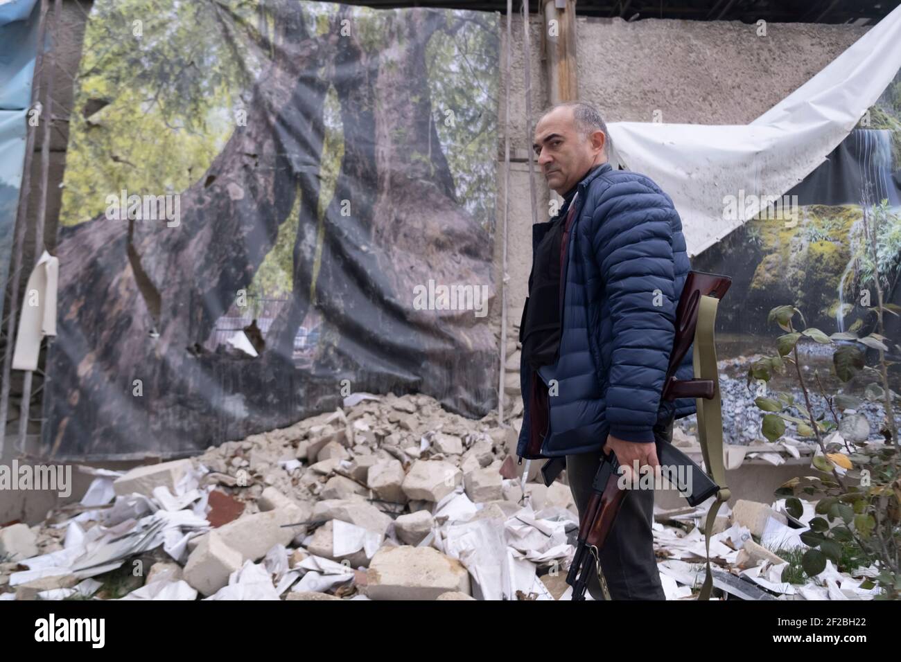 STEPANAKERT, NAGORNO KARABAKH - NOVEMBRE 04: Tevan Poghosyan, consigliere del presidente armeno ed ex membro del Parlamento armeno, armato di un fucile AK-47 Kalashnikov, si trova in mezzo al relitto di un edificio distrutto da uno sciopero militare azero a Stepanakert, capitale de facto dell'autoproclamata Repubblica di Artsakh o Nagorno-Karabakh, De jure parte della Repubblica di Azerbaigian il 04 novembre 2020. I combattimenti tra l'Armenia e l'Azerbaigian sul Nagorno-Karabakh conosciuto anche come la Repubblica Artsakh rieruttarono alla fine di settembre in una guerra di sei settimane con entrambi i paesi accusando ogni othe Foto Stock