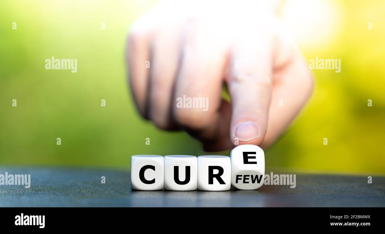 La mano gira i dadi e cambia la parola "curfew" in "cure". Foto Stock
