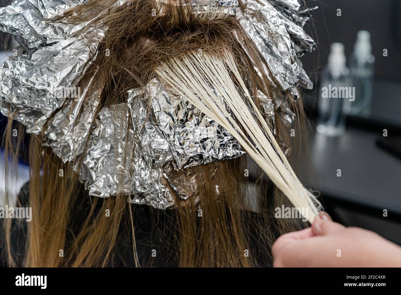 Stylist dei capelli che controlla i capelli durante il processo di sbianca. Illuminazione trendy dei capelli con tecnica shatush. Foto Stock