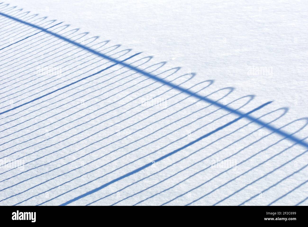 Il modello geometrico regolare di ombre gettate da una recinzione attraverso un campo di neve intatto. Foto Stock