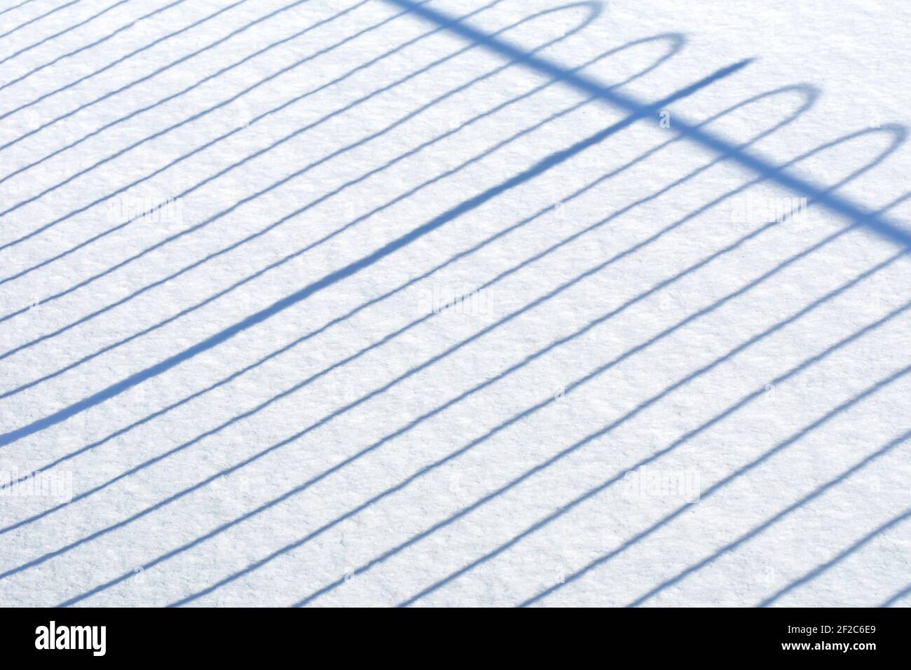 Primo piano del modello geometrico regolare di ombre gettate da una recinzione attraverso un campo di neve intatto. Foto Stock
